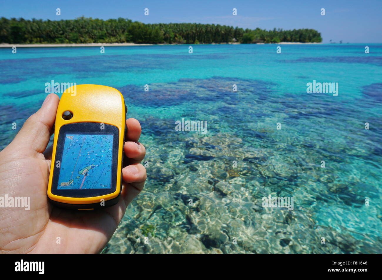 Navigatore satellitare GPS in mano sul mare sfocate con barriera corallina sotto la superficie dell'acqua e un'isola all'orizzonte, scena naturale Foto Stock