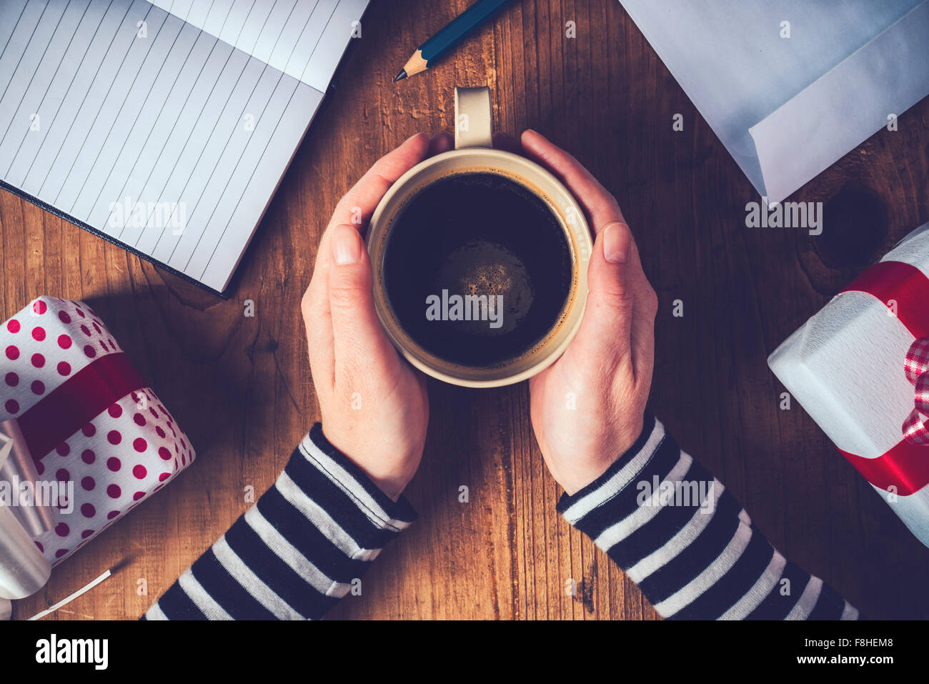 Caffè di natale, vista dall'alto di mani femminili in possesso di una tazza di caffè caldo drink sul tavolo di legno con i regali di Natale in scatole, retro ton Foto Stock