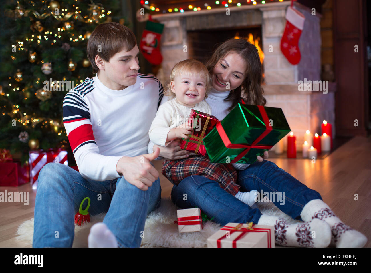 La famiglia felice - padre, madre e figlio seduti con doni vicino albero di Natale e camino Foto Stock