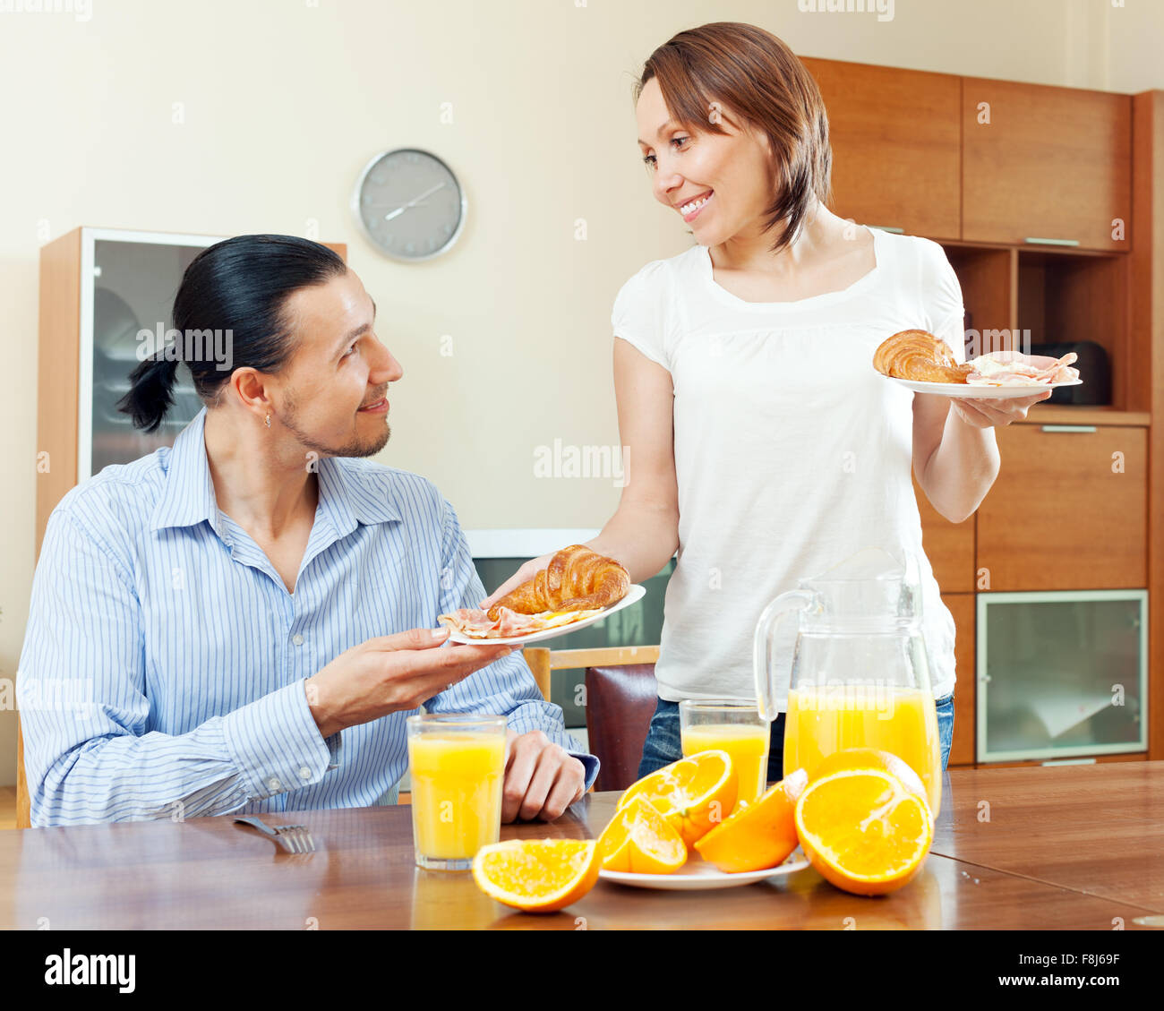 Donna sorridente serve croissants e uova strapazzate con il suo amato uomo nella mattina la prima colazione Foto Stock