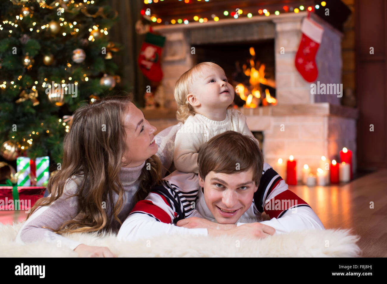 La famiglia felice con il piccolo figlio che giace nei pressi di albero di Natale e camino Foto Stock