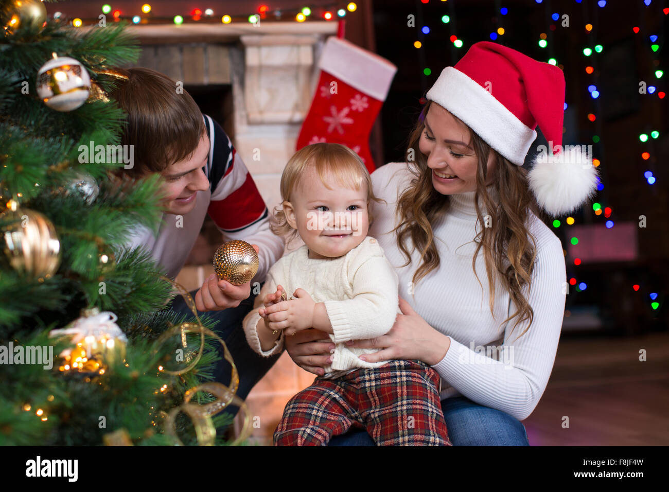 La famiglia felice con bambino decorare albero di Natale davanti al caminetto in soggiorno Foto Stock
