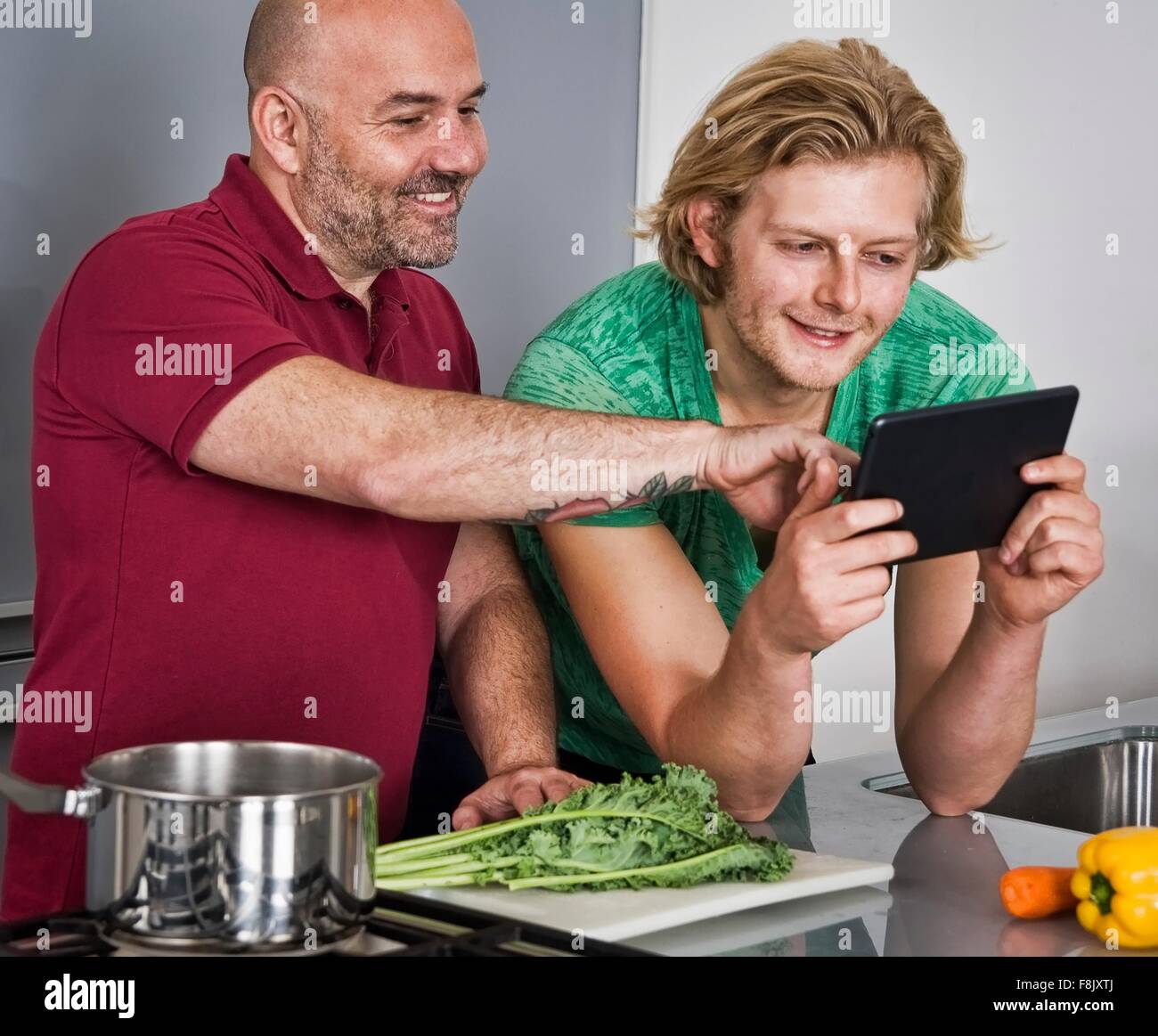 Giovane maschio con tavoletta digitale mentre la preparazione di cibo in cucina Foto Stock