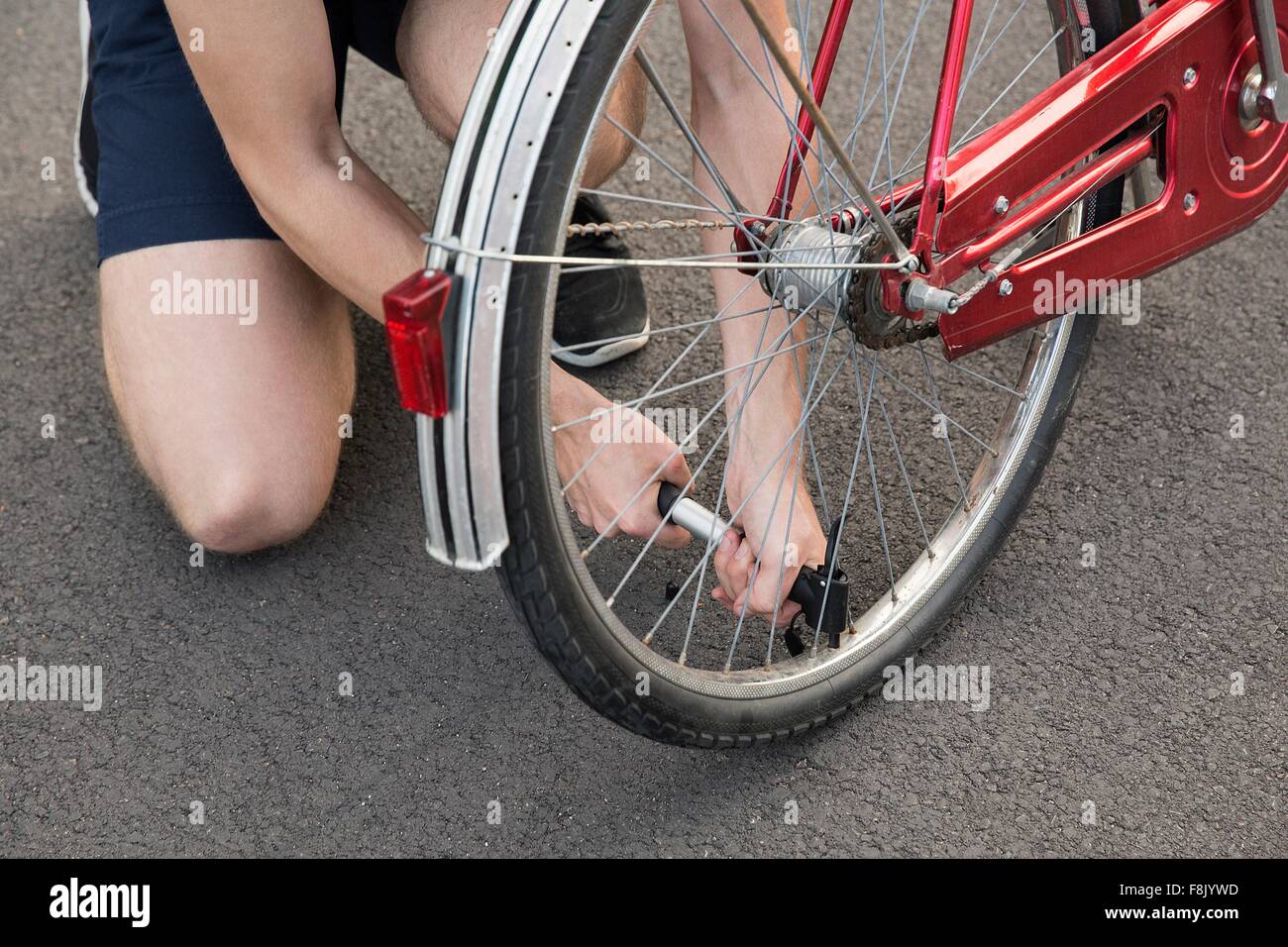 Vista ritagliata della giovane inginocchiarsi di gonfiaggio di pneumatico per bicicletta Foto Stock