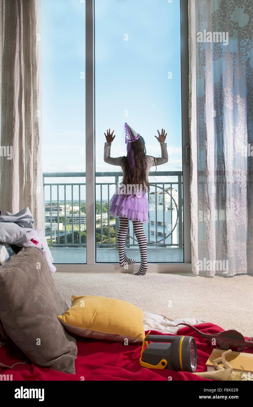 Giovane ragazza che indossa abiti di festa, guardando fuori della finestra, vista posteriore Foto Stock