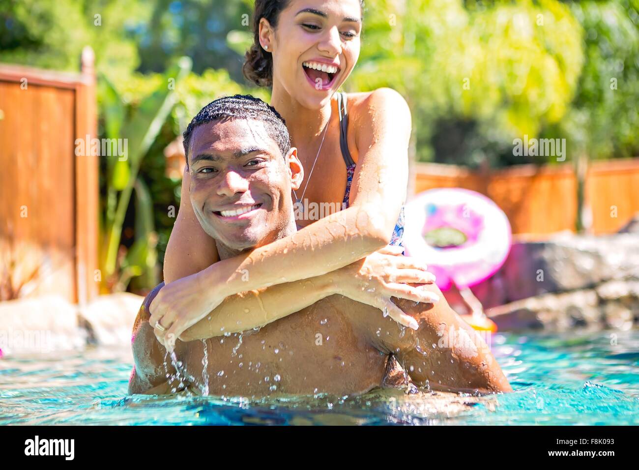 Metà uomo adulto che trasportano giovane donna sul retro in piscina guardando sorridente della fotocamera Foto Stock