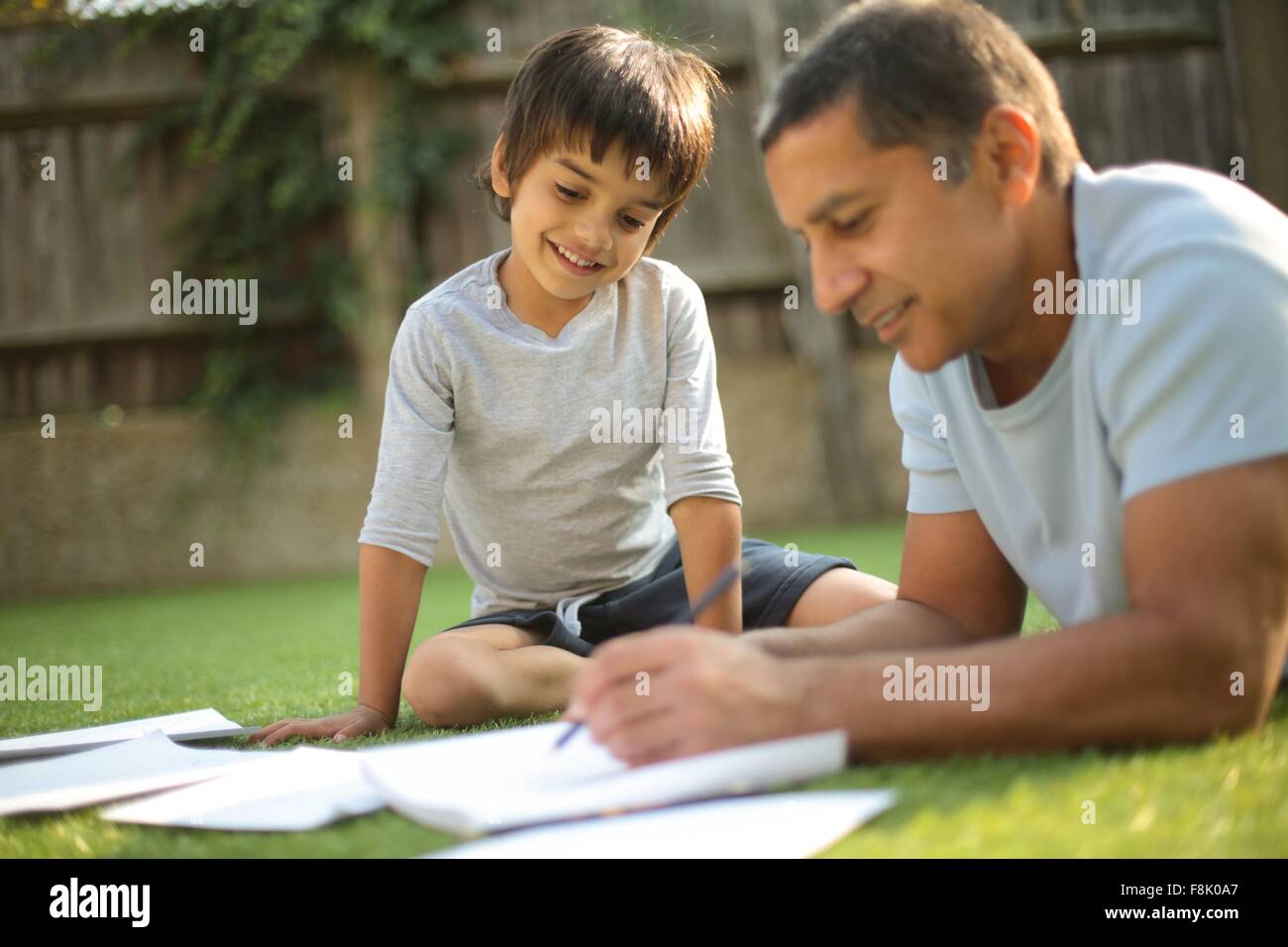 Ragazzo seduto sull'erba la visione di padre fare carte guardando giù sorridente Foto Stock