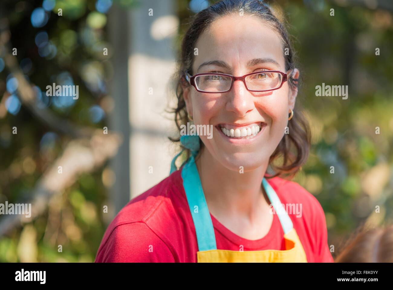 Ritratto di donna matura che indossa il grembiule e bicchieri guardando sorridente della fotocamera Foto Stock