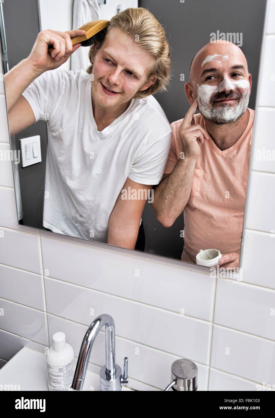 Specchio bagno immagine del giovane maschio della rasatura e spazzolare i capelli Foto Stock