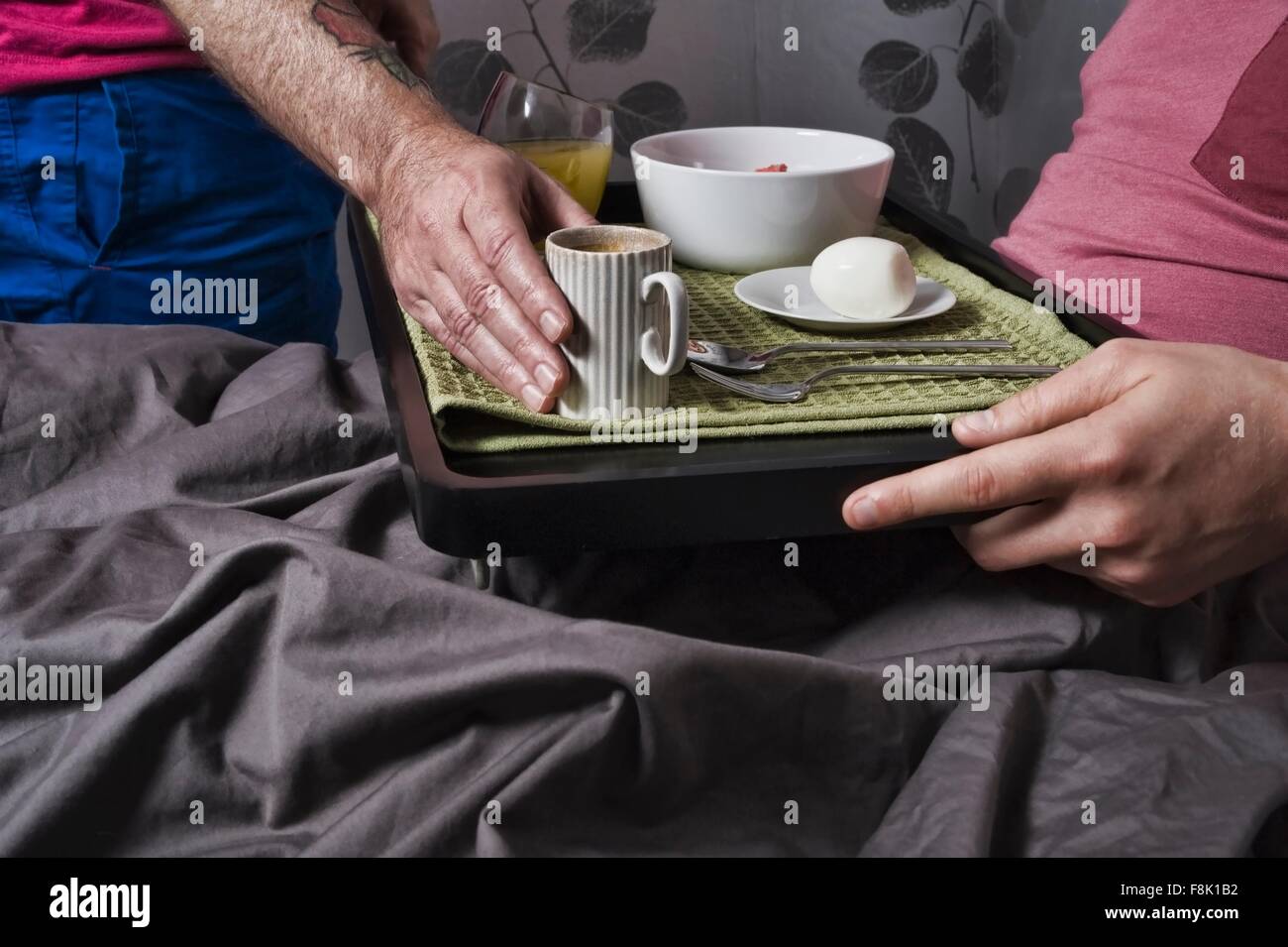 Close up uomo immissione tazza da caffè sul vassoio di prima colazione al ragazzo nel letto Foto Stock