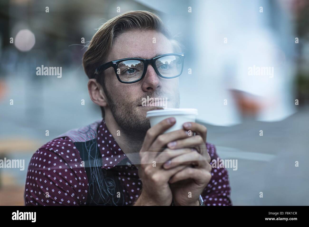 Triste giovane impreditore dietro la finestra della città a bere il caffè da asporto Foto Stock