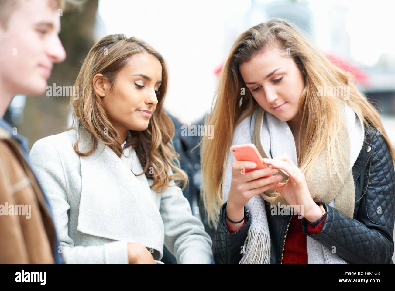Giovane donna con amici prendendo la lettura di testi dello smartphone su strada Foto Stock
