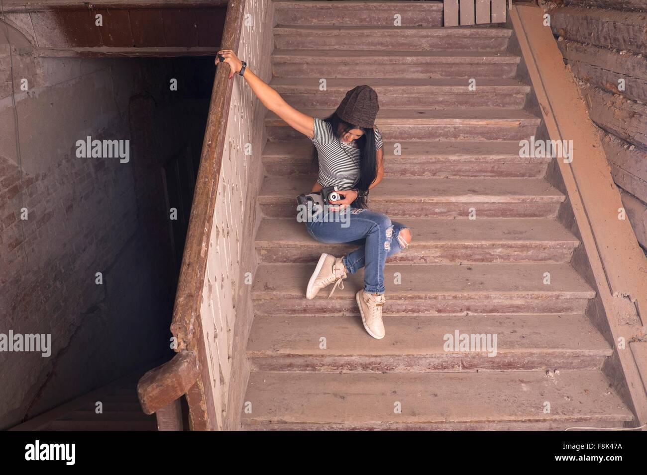 Femmina giovane fotografo preparazione fotocamera su scale nel vecchio edificio industriale Foto Stock