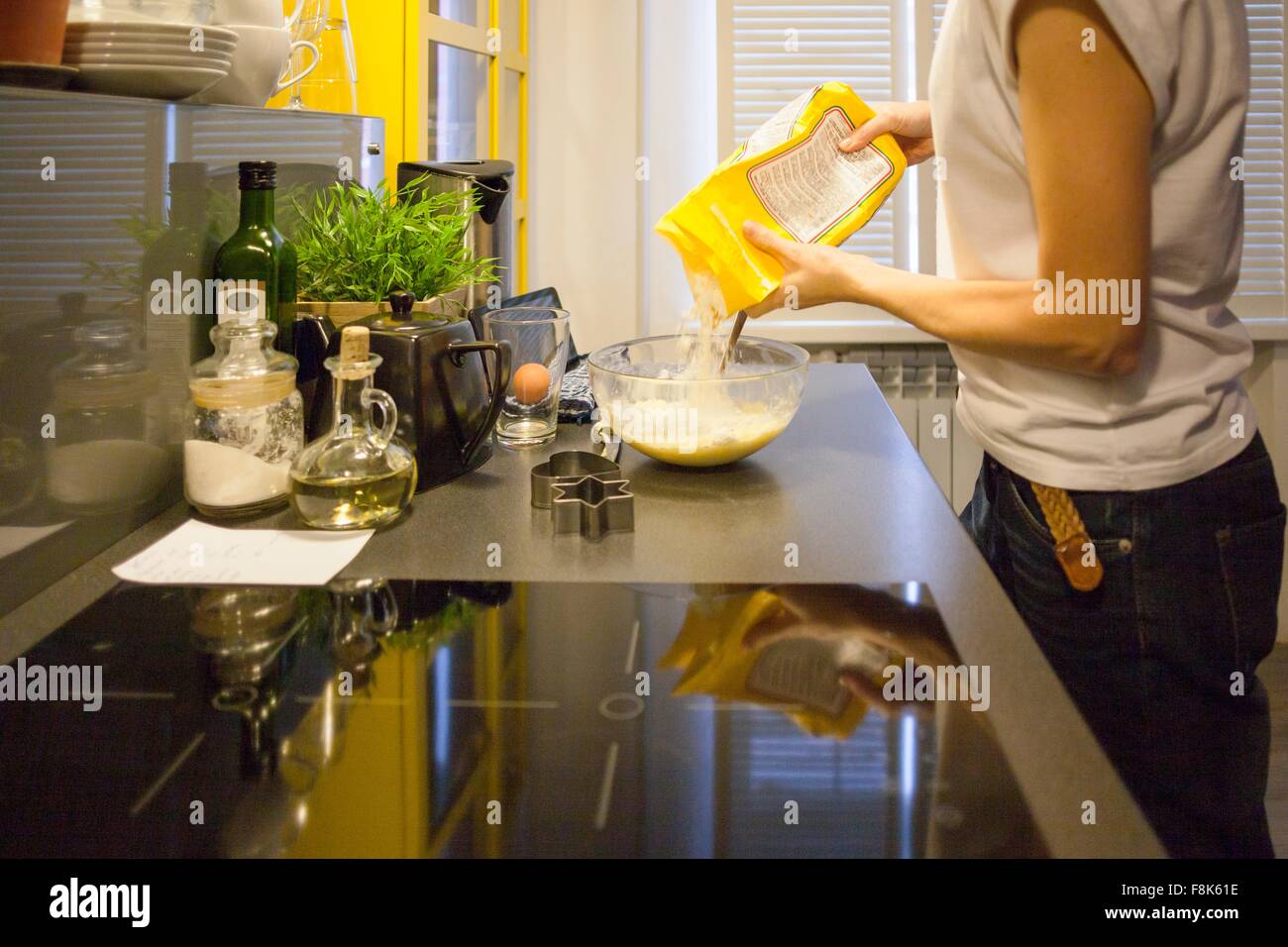 Metà donna adulta versando la farina nel recipiente di miscelazione al banco di cucina Foto Stock