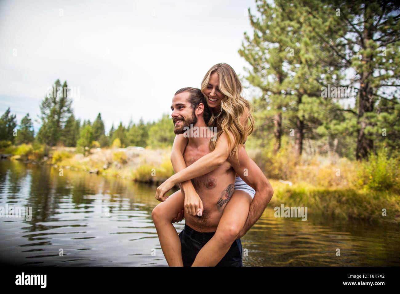 Giovane uomo dando ragazza piggyback nel fiume, Lake Tahoe, Nevada, STATI UNITI D'AMERICA Foto Stock