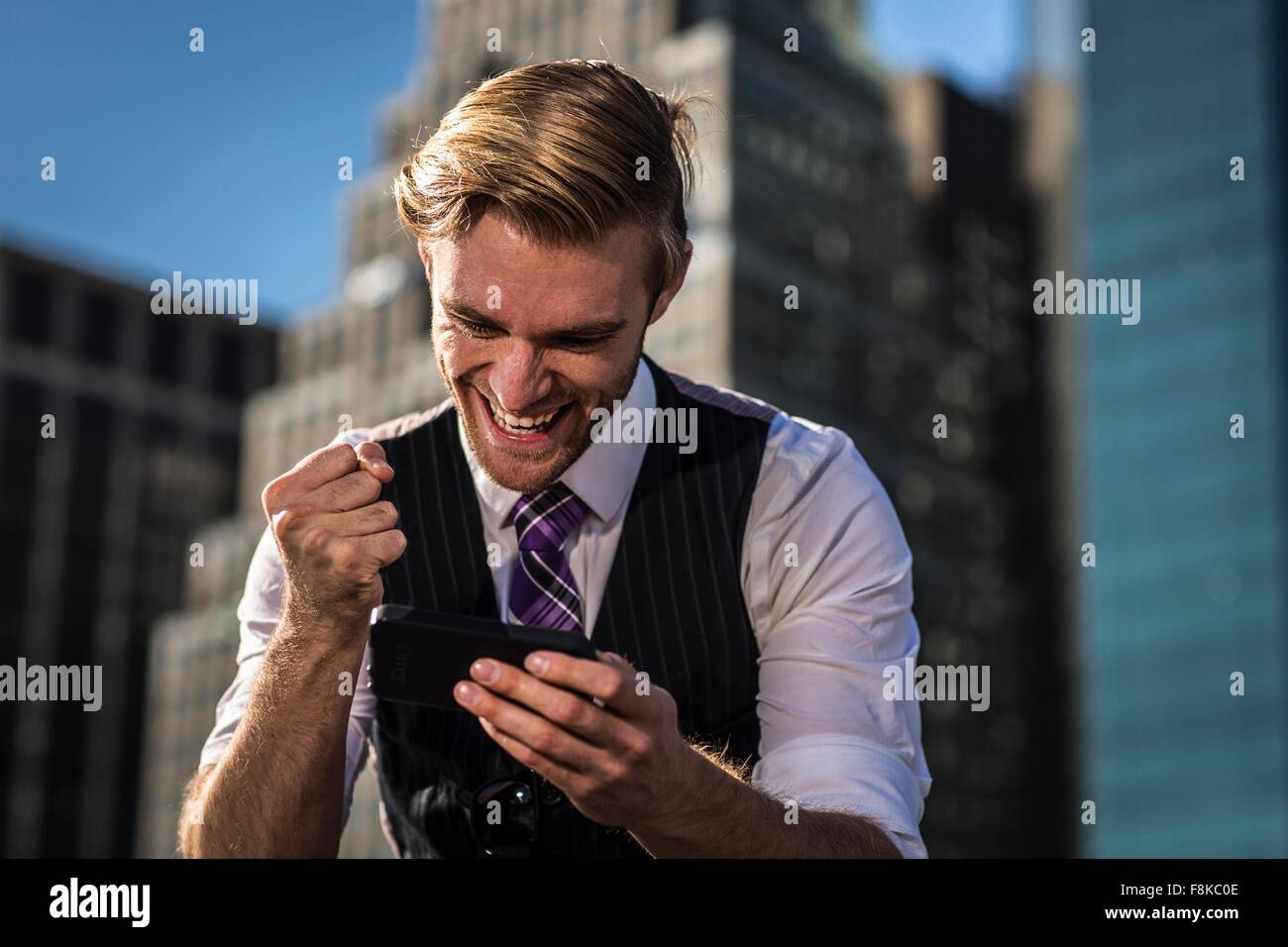Giovane imprenditore di fronte all ufficio del pugno di aggraffaggio a smartphone, New York, Stati Uniti d'America Foto Stock