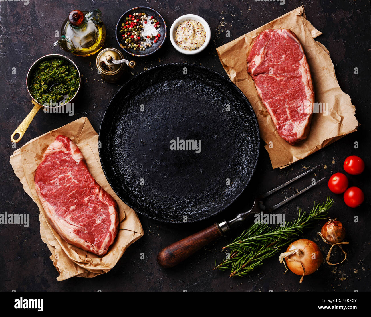 Materie carni fresche controfiletto bistecche con ingredienti intorno a padella su sfondo scuro Foto Stock