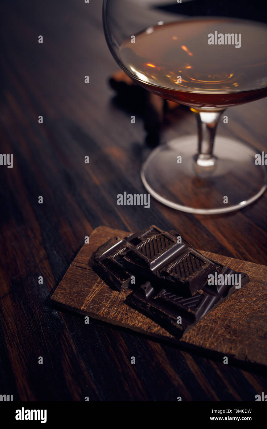 Bicchiere di brandy su un tavolo di legno con cioccolato e sigaro. sfondo grigio. Foto Stock