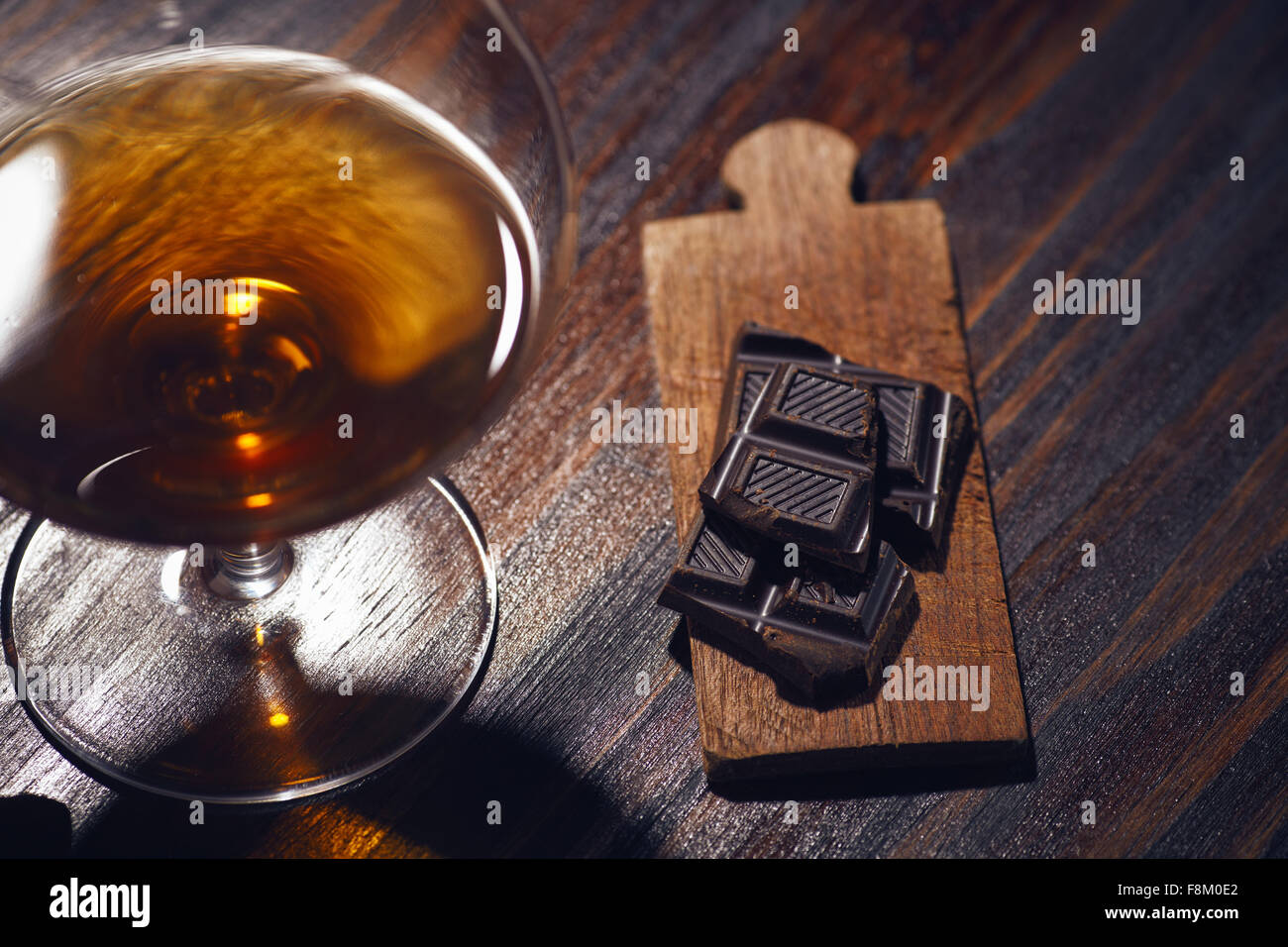 Bicchiere di brandy su un tavolo di legno con cioccolato e sigaro. sfondo grigio. Foto Stock