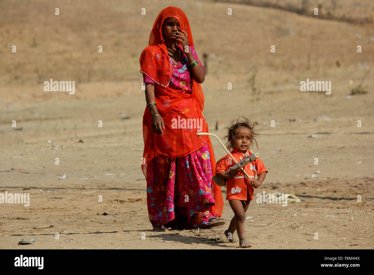 Pushkar, India, 28 Novembre 2012: un povero indiano madre orange vestito con suo figlio, in piedi sulla sabbia in Pushkar Foto Stock