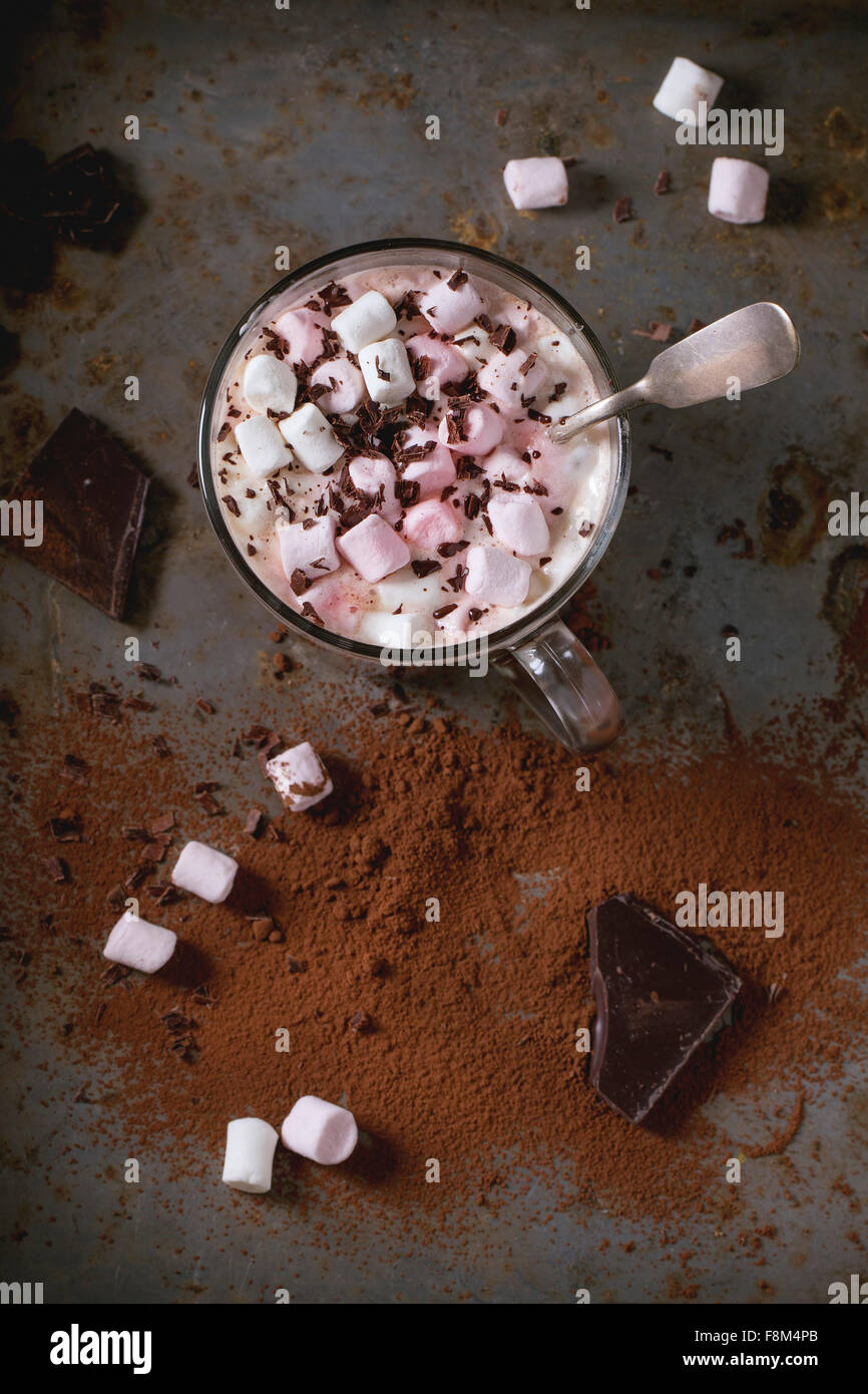 Vetro tazza di cioccolata calda con fusione marshmallows, vintage cucchiaio d'argento e la polvere di cacao ruggine sulla superficie metallica. Rustico scuro Foto Stock