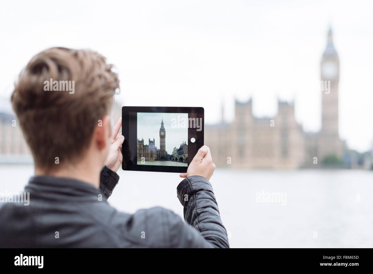 Vista posteriore del giovane uomo a fotografare il Big Ben sulla tavoletta digitale, London, England, Regno Unito Foto Stock