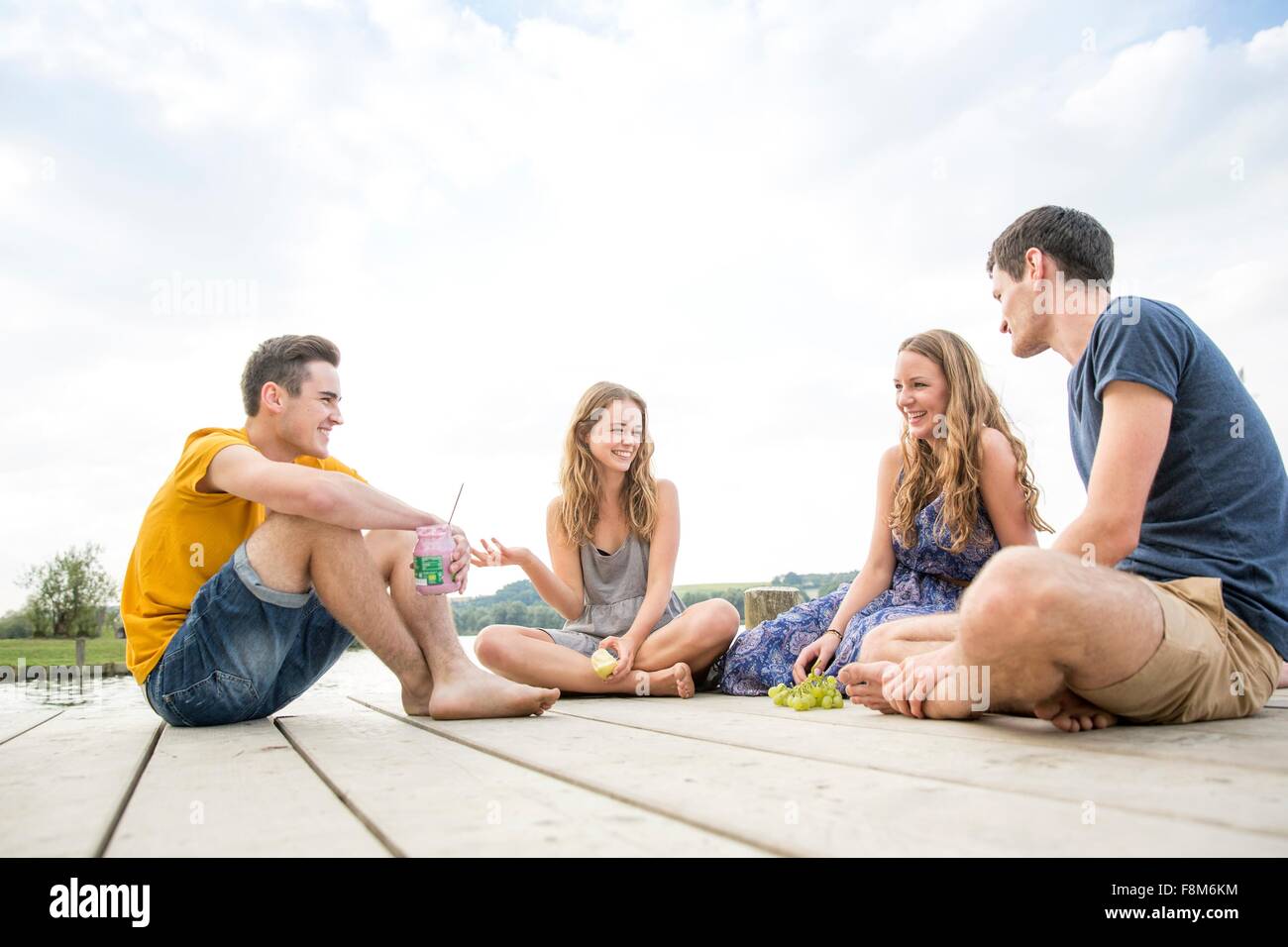 Un gruppo di giovani adulti seduti sul molo, rilassante Foto Stock