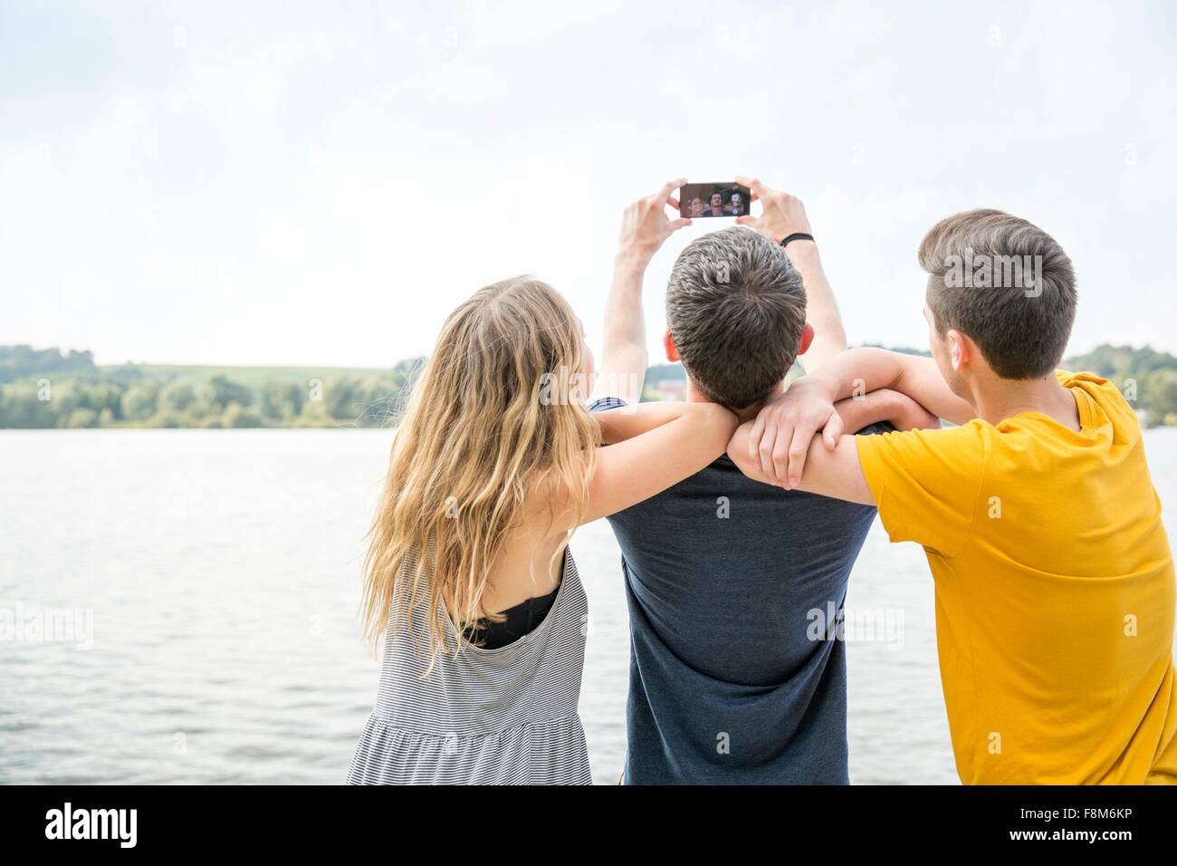 Tre giovani adulti tenendo autoscatto utilizzando lo smartphone, vista posteriore Foto Stock
