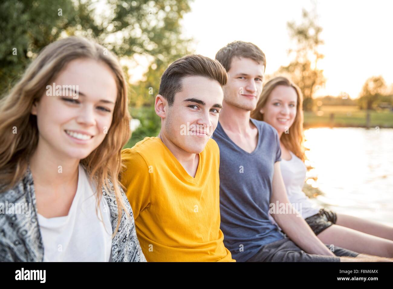 Ritratto di gruppo di amici seduti accanto al lago, sorridente Foto Stock