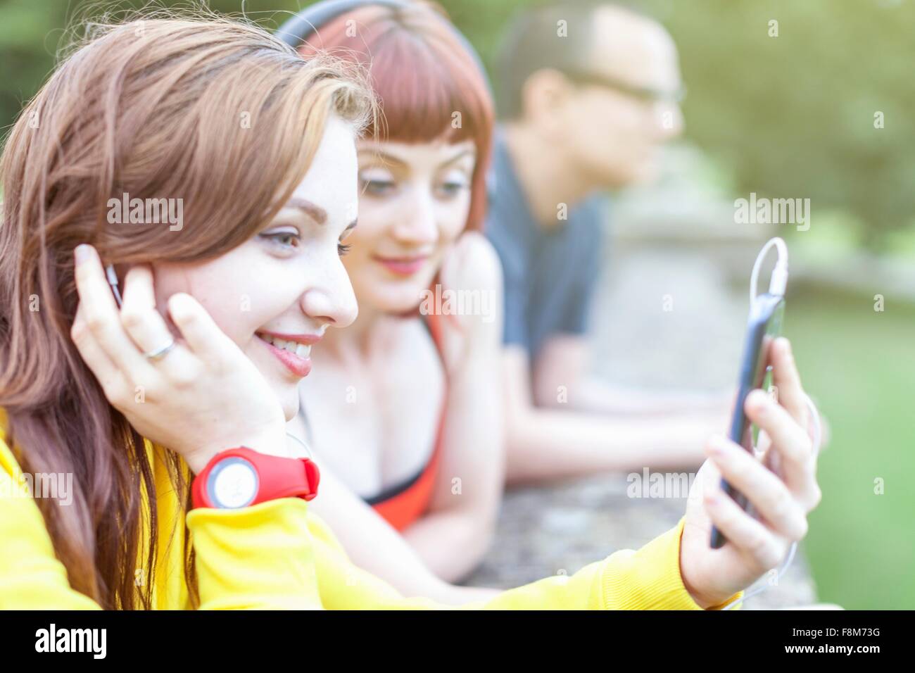 Giovani donne utilizza lo smartphone, appoggiata sulla parete bassa Foto Stock