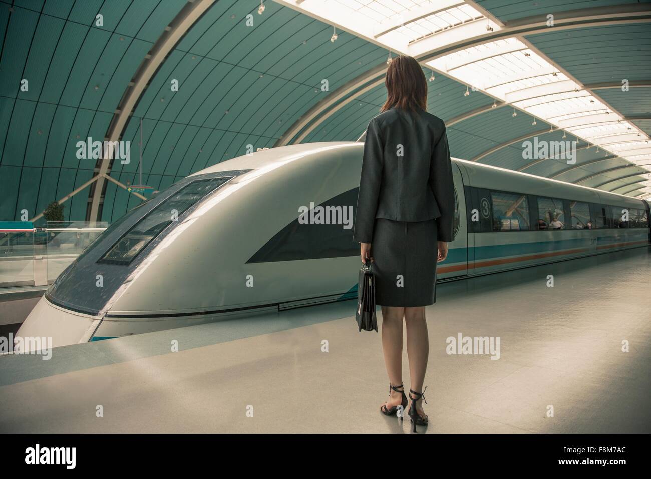 Business donna in attesa di un treno su piattaforma ferroviaria, Shanghai, Cina Foto Stock