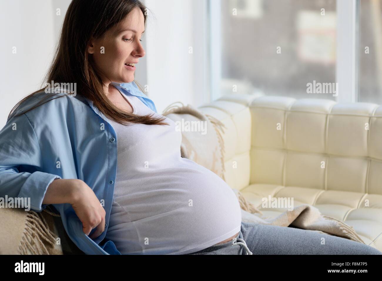 Donna incinta seduta sul divano Foto Stock