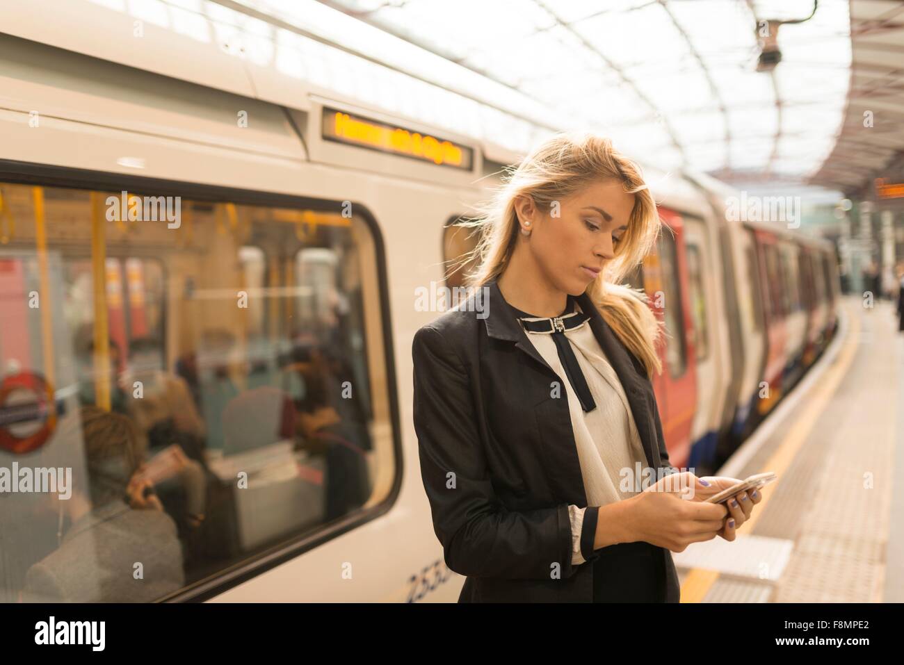 Business donna texting sulla piattaforma, la stazione della metropolitana di Londra, Regno Unito Foto Stock