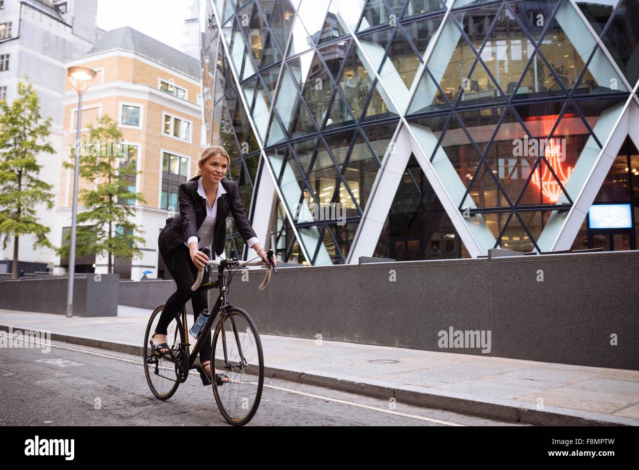 Imprenditrice sulla bici passando 30 St Mary Axe, London, Regno Unito Foto Stock
