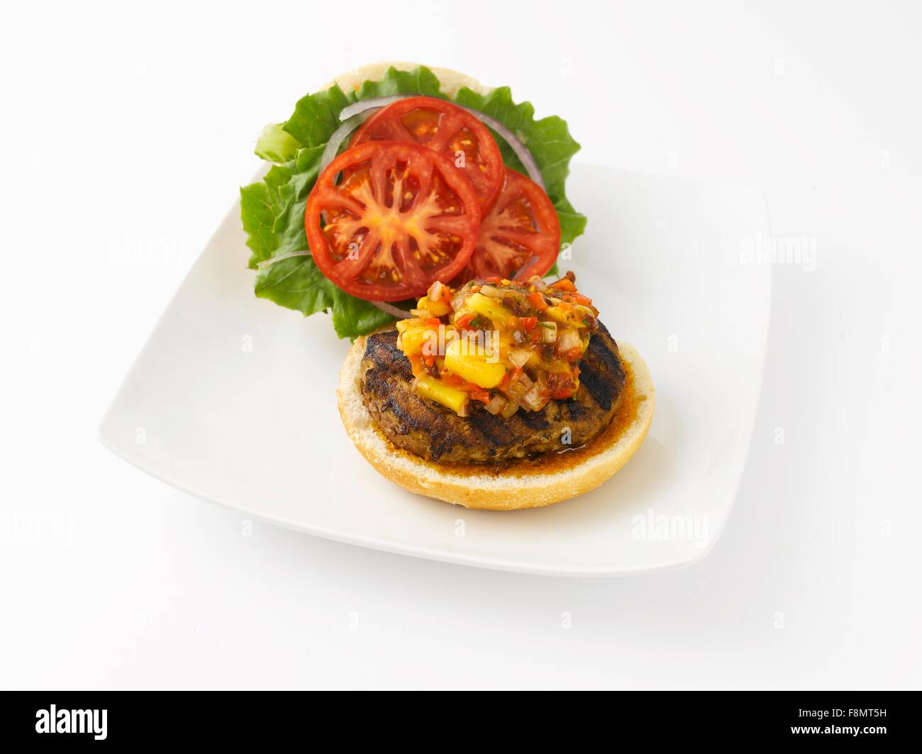 Aprire il tacchino alla griglia Burger con salsa di mango, pomodori e lattuga; sulla piastra bianca su sfondo bianco Foto Stock