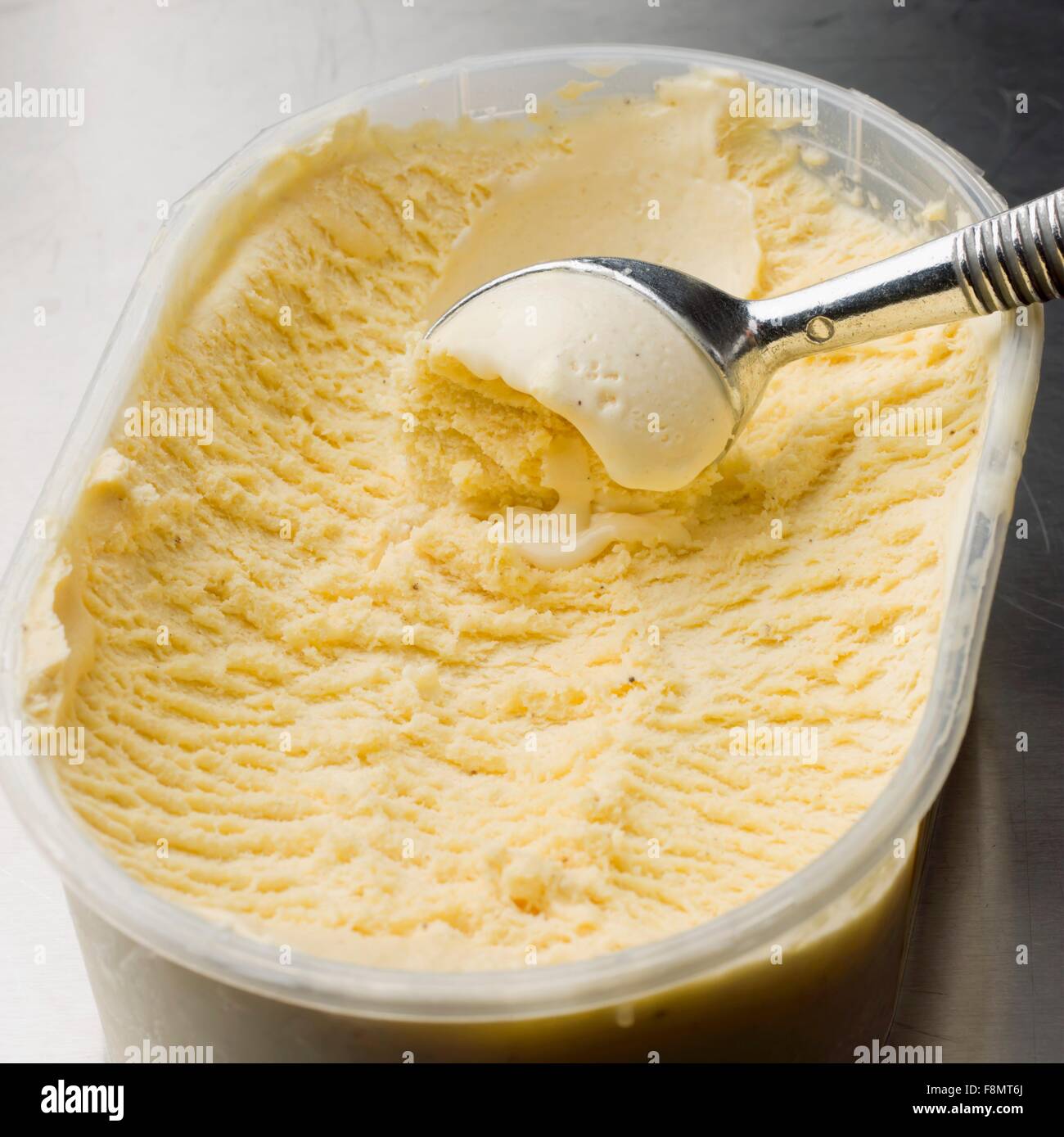 Gelato alla vaniglia in un contenitore di plastica con un gelato convogliatore Foto Stock