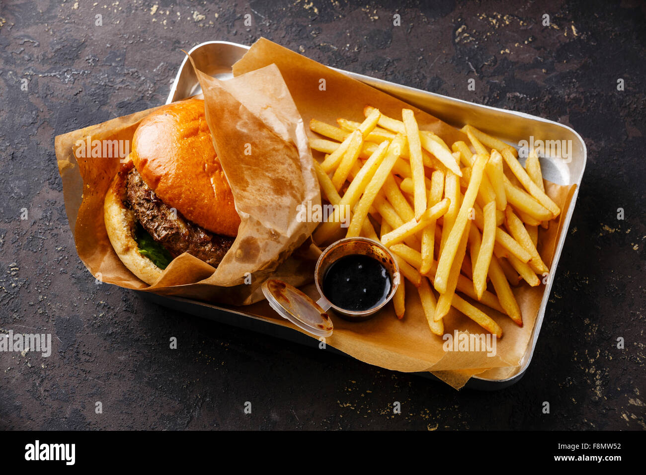 Burger con carne e patate fritte nel vassoio di alluminio su sfondo scuro Foto Stock
