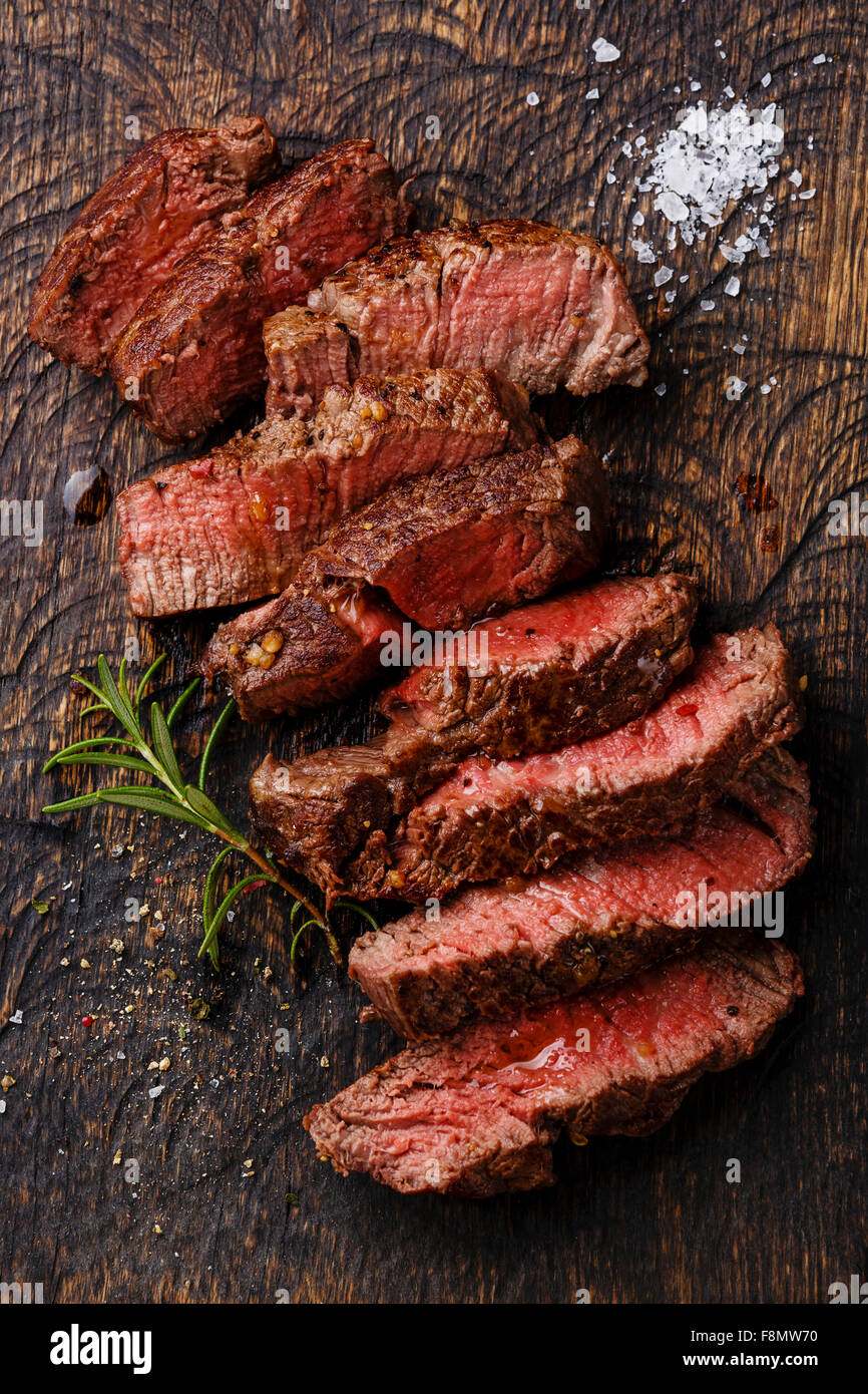 Fette di mezzo raro grigliate di carne di manzo sul tagliere di legno sfondo Foto Stock