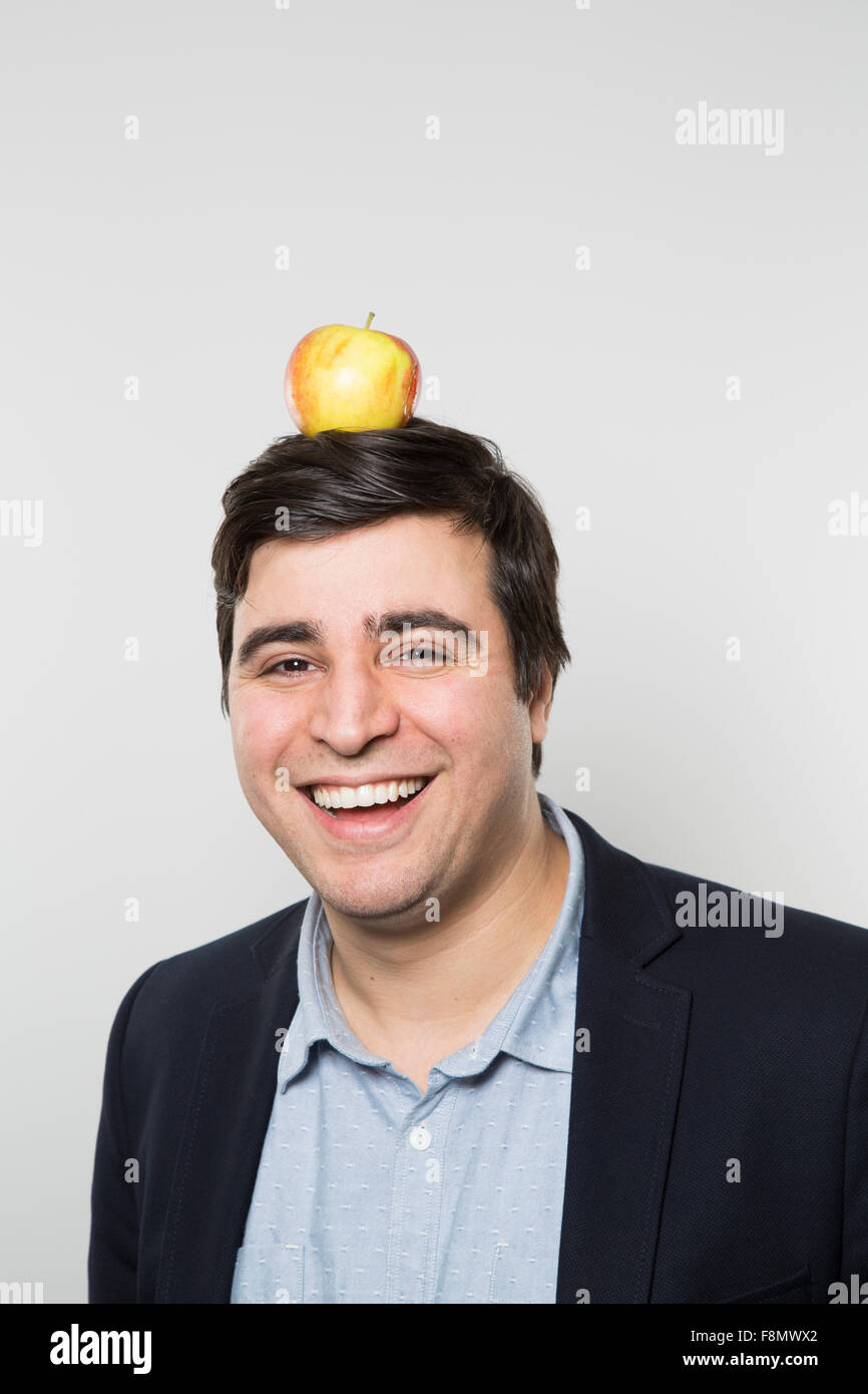 Dai capelli scuri imprenditore europeo con un piccolo apple sulla cima della sua testa e viso sorridente sorge nella parte anteriore di un gradiente dello sfondo Foto Stock