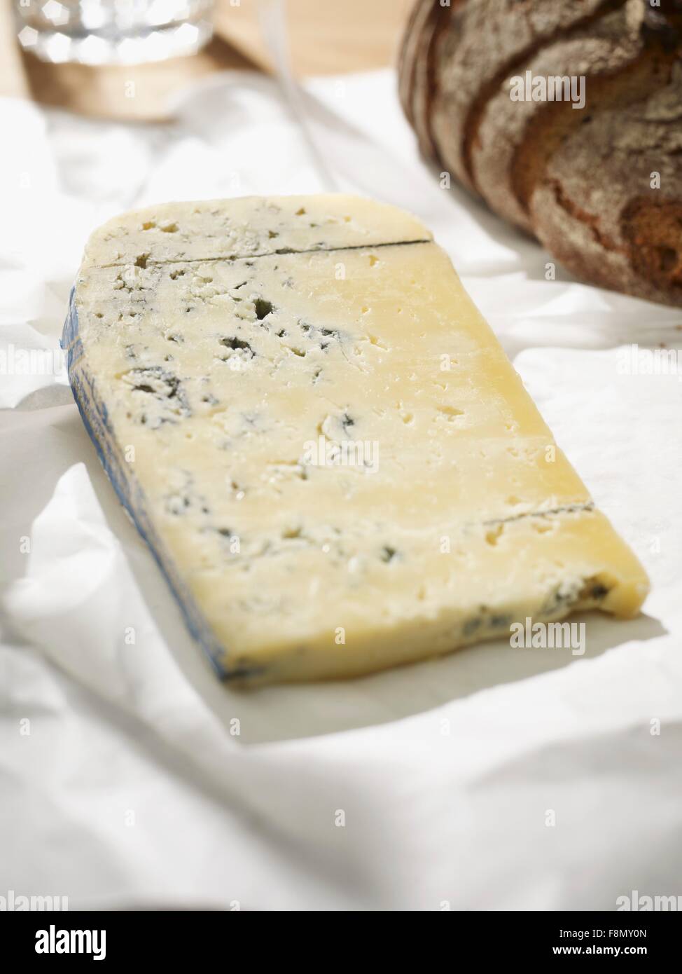 Formaggio blu su bianco carta da forno; in background, pane rustico Foto Stock