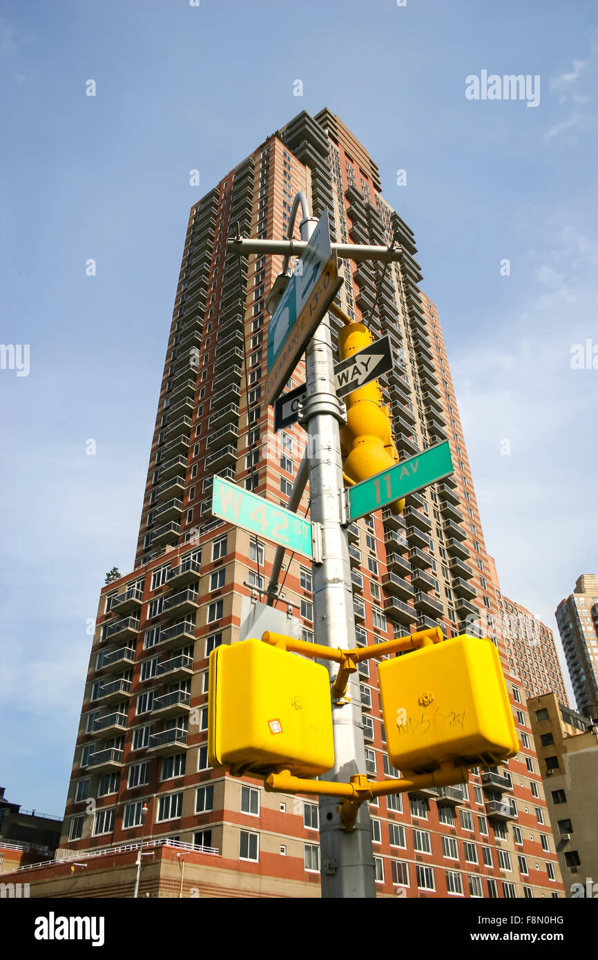 Un basso angolo di visione di un grattacielo e una lampada posta con cartelli stradali in intersezione di 42nd Street e 11th Avenue a Manhattan Foto Stock