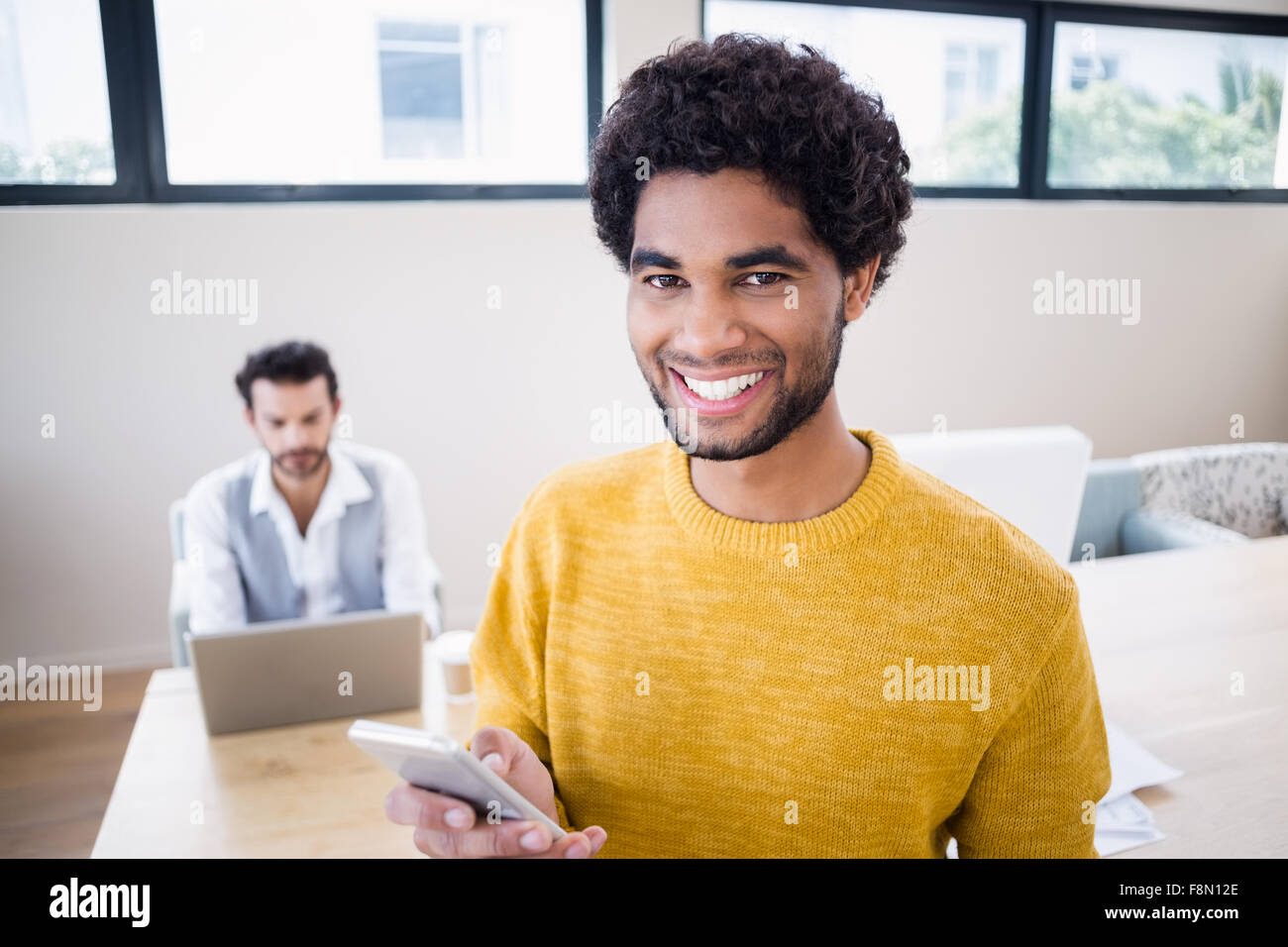 Uomo sorridente utilizza lo smartphone con il partner in background Foto Stock