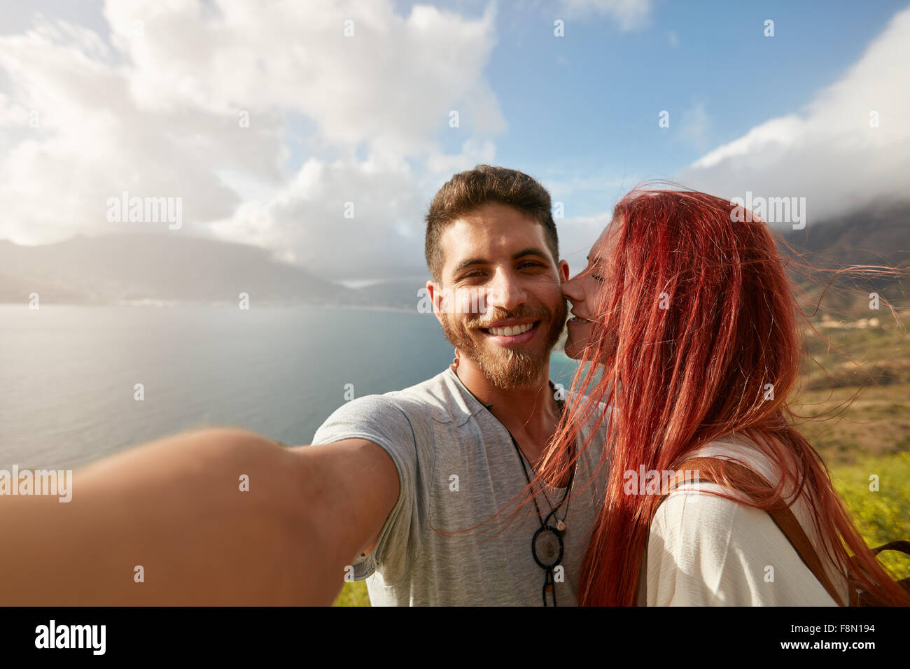 Coppia giovane prendendo un selfie all'esterno. POV shot uomo in possesso di una fotocamera e prendendo un autoritratto con la donna baciare lui. Foto Stock
