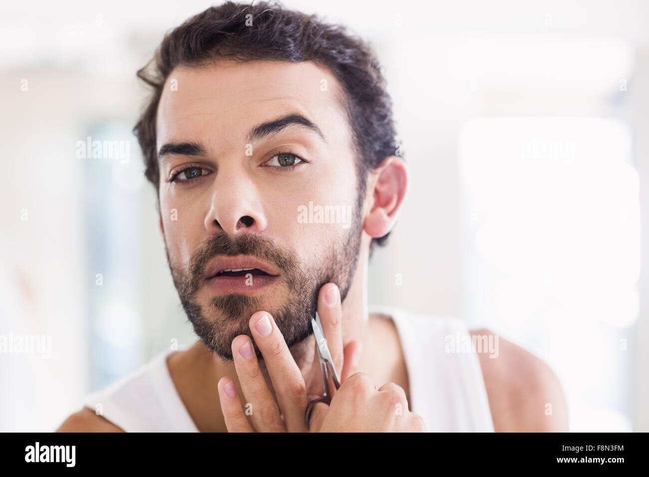 Uomo concentrato il suo taglio di barba con le forbici Foto Stock