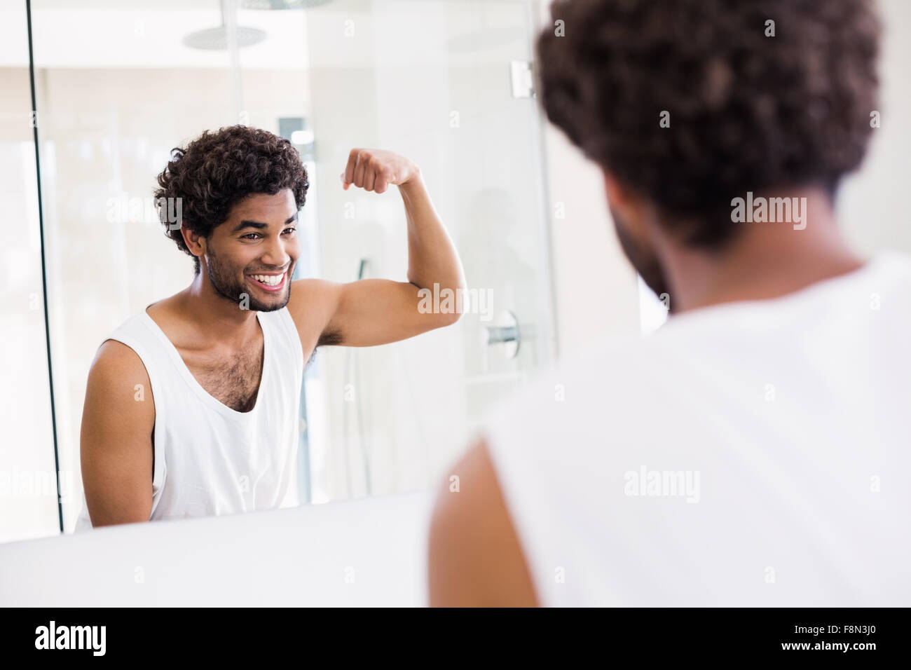 Uomo sorridente guardando al suo bicipite in specchio Foto Stock