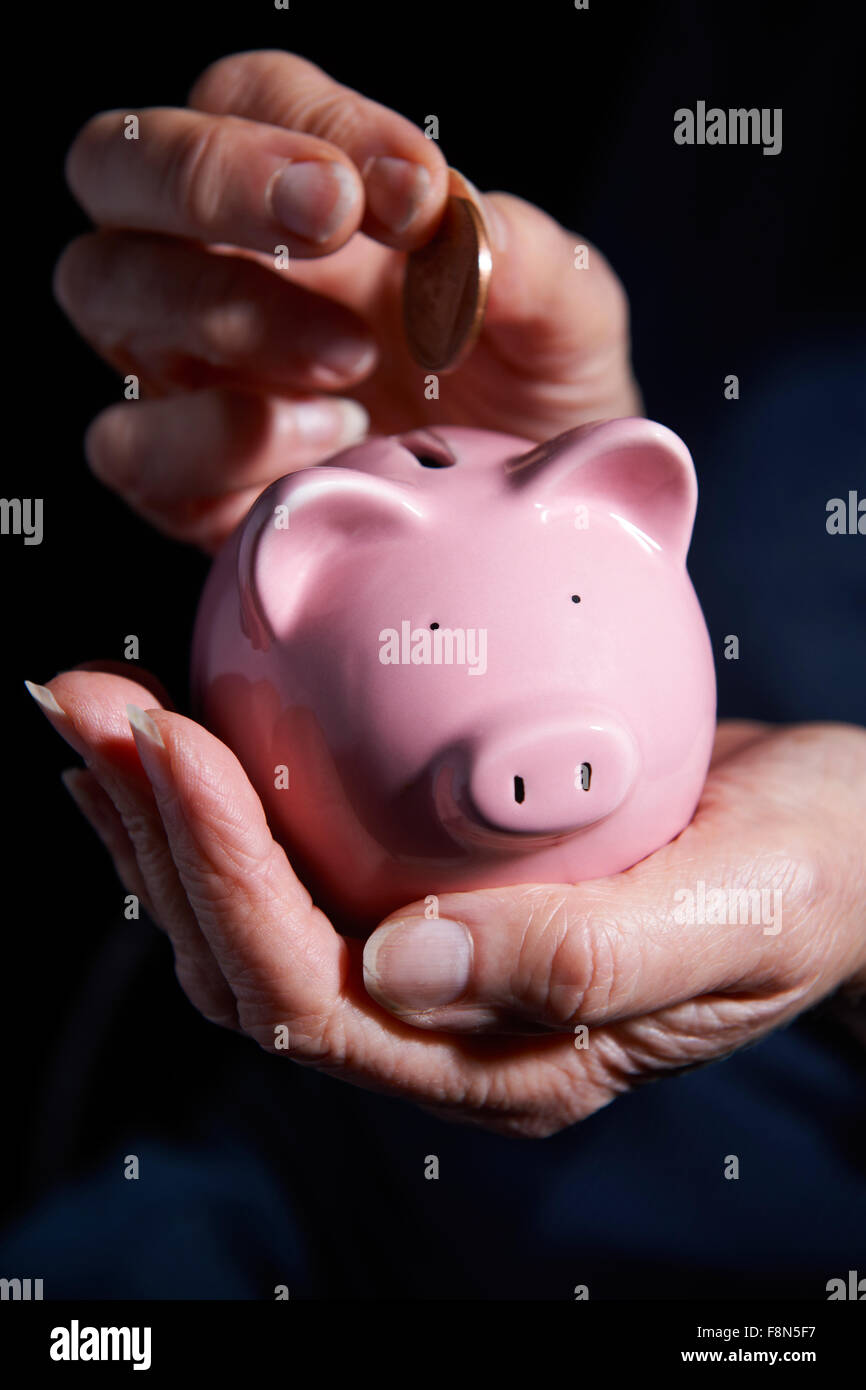 Senior donna mettendo monete nel salvadanaio Foto Stock