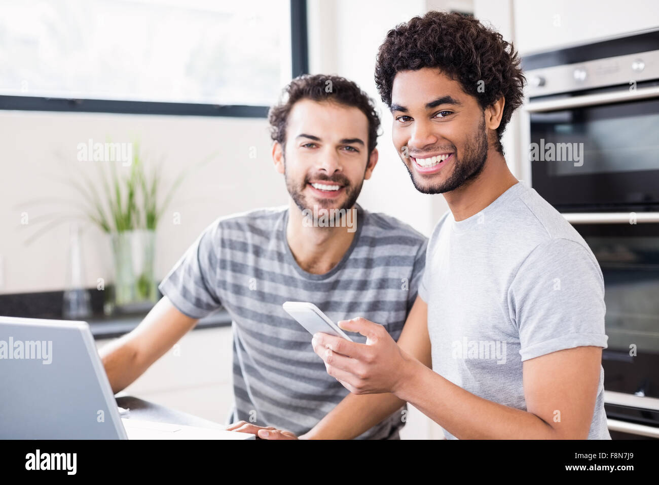 Felice coppia gay utilizzando la tecnologia in cucina Foto Stock