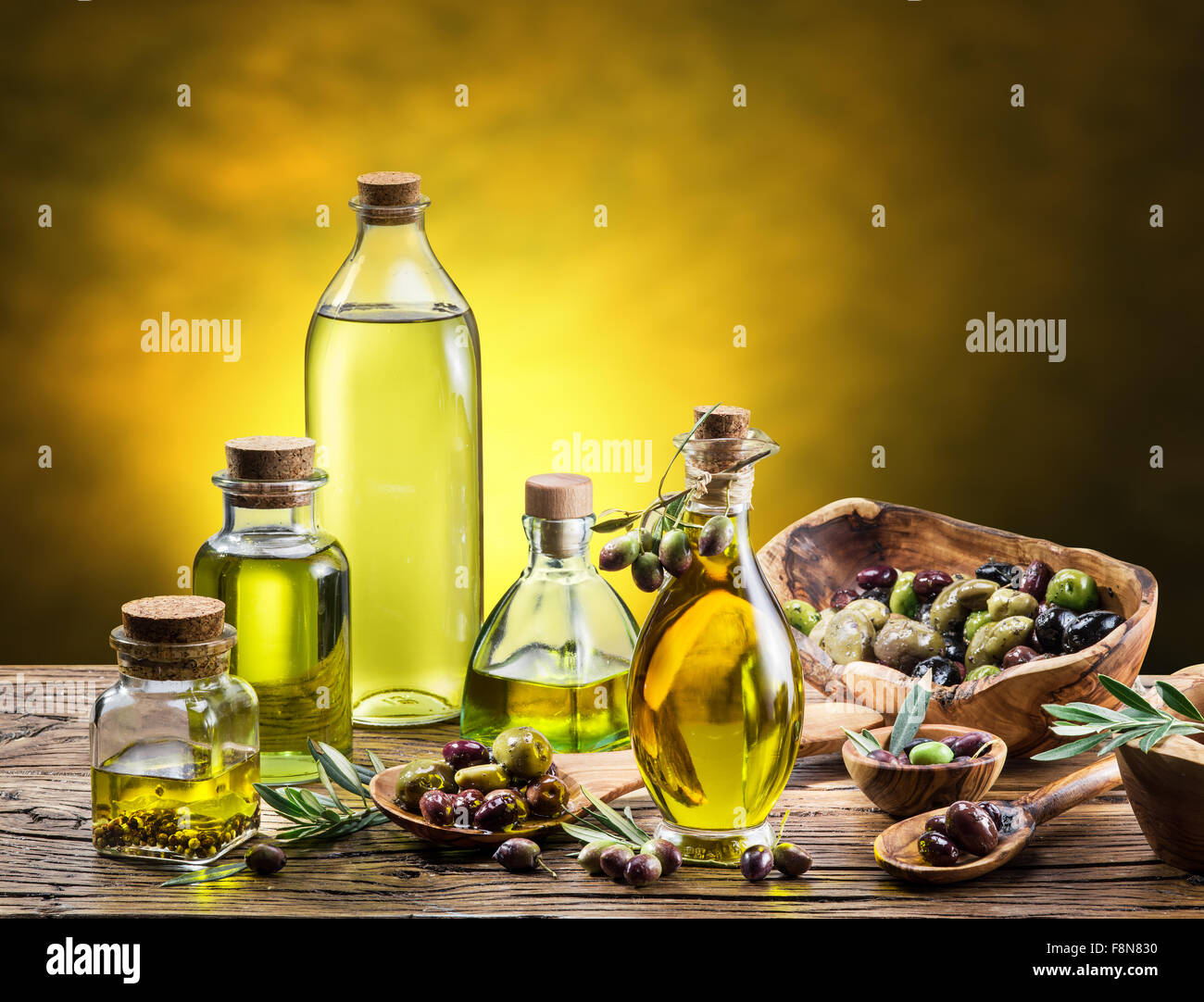 Bottiglie di vetro di olio di oliva e pochi acini sul tavolo di legno. Studio shot. Foto Stock
