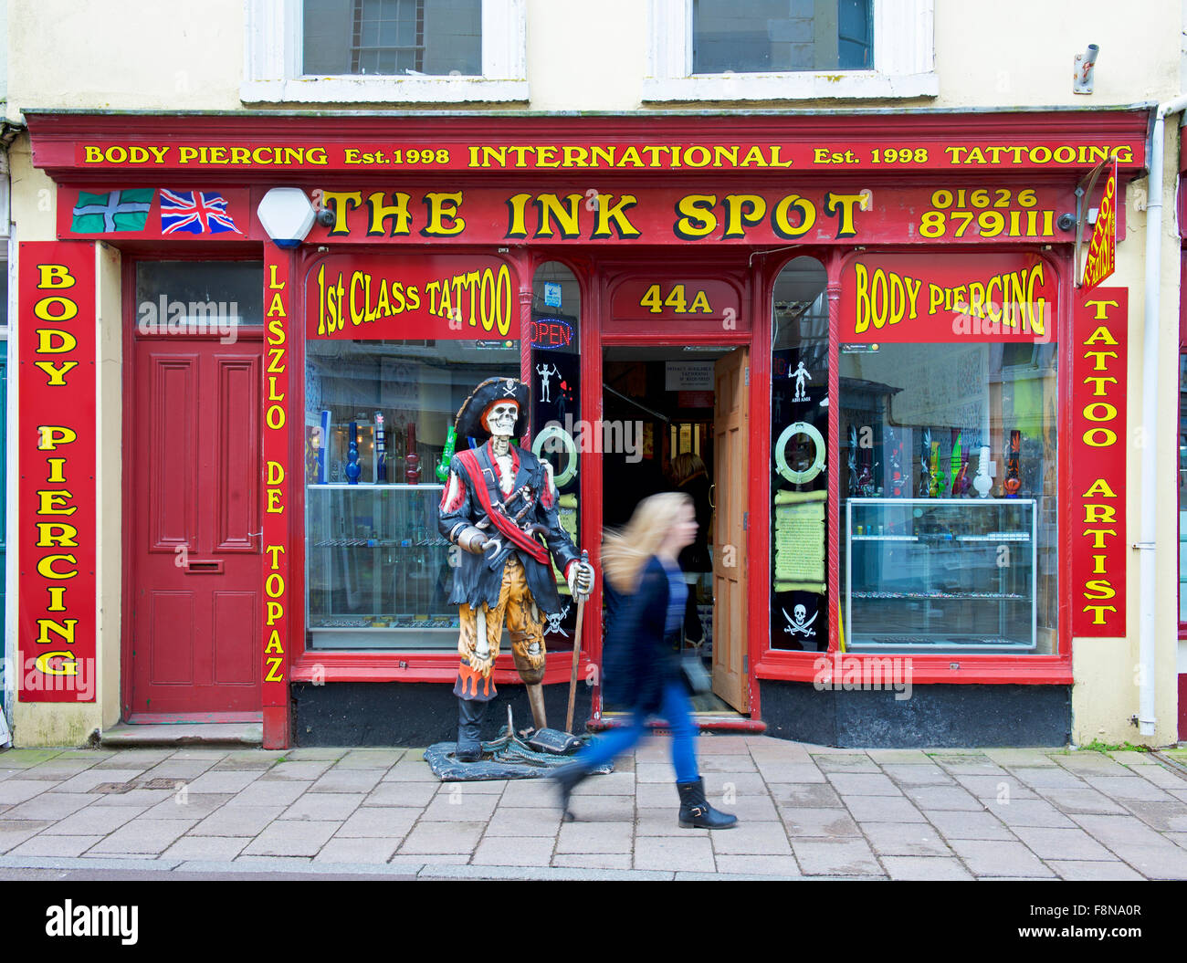 Ragazza camminare oltre la macchia di inchiostro, tatuaggi e piercing shop, Teignmouth, Devon, Inghilterra, Regno Unito Foto Stock