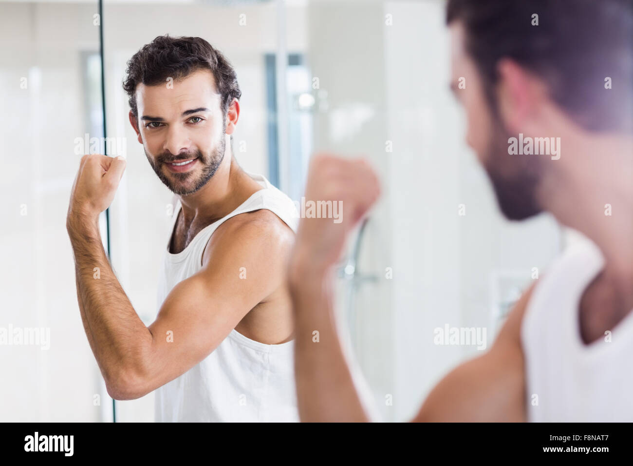 Uomo sorridente guardando al suo bicipite in specchio Foto Stock